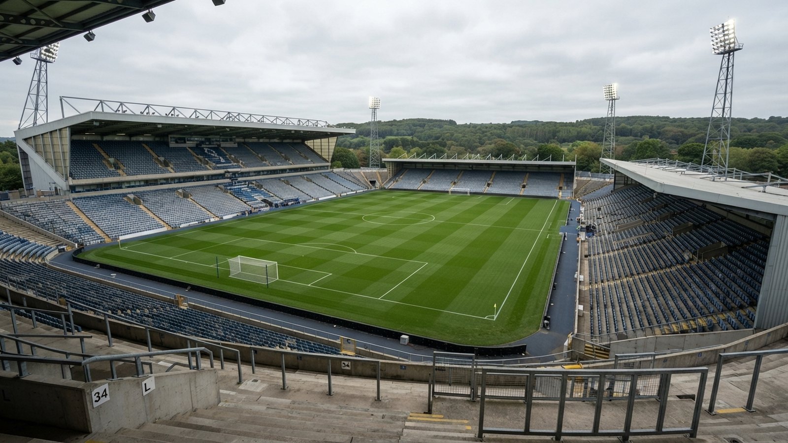 Prázdný fotbalový stadion s osvětlovacími stožáry a zalesněnými kopci v pozadí